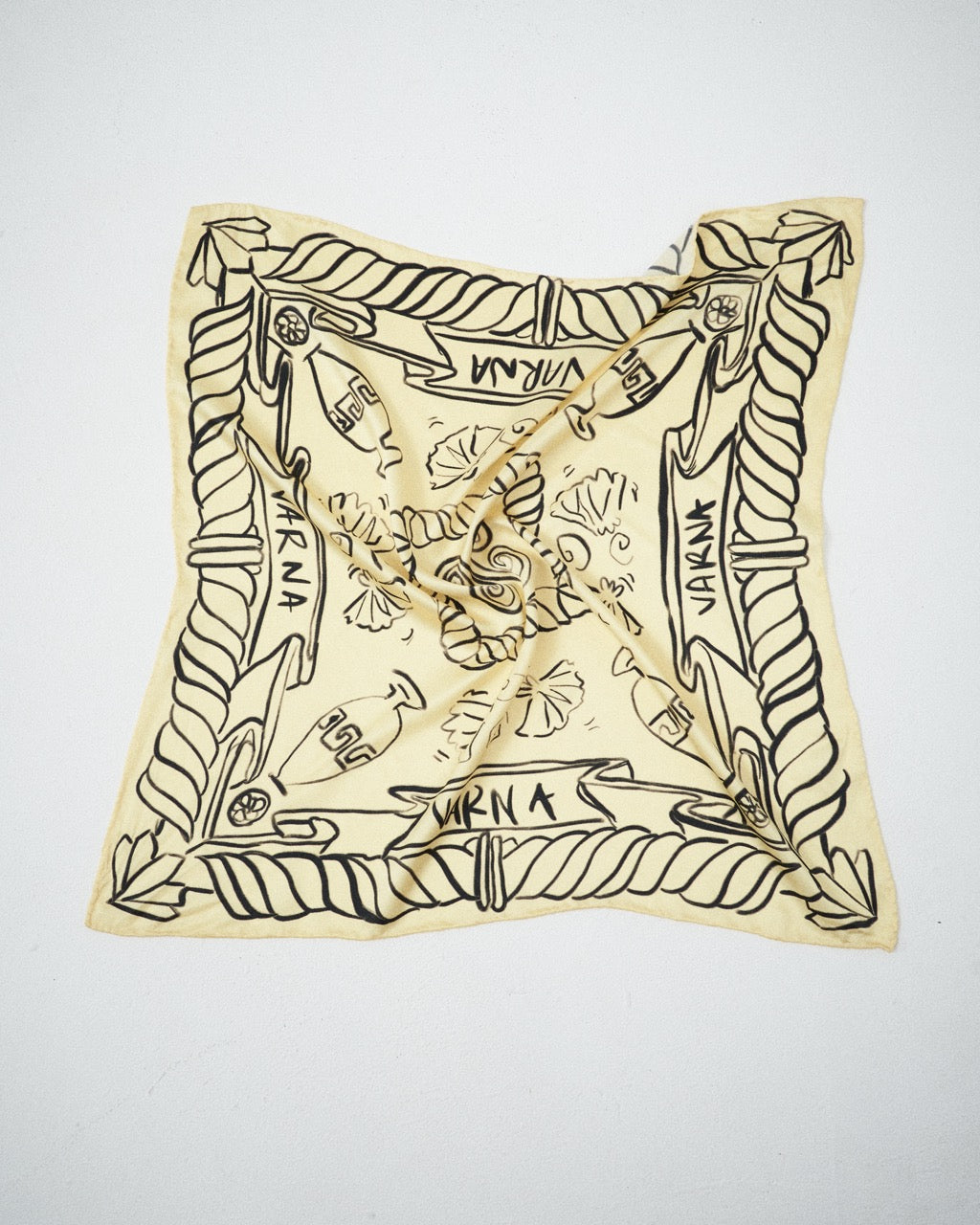 Flat lay of the Artefact Silk Scarf in soft yellow with black VARNA hand-drawn artwork