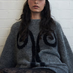 Editorial mood shot of the VARNA Maris Knit Top in charcoal — oversized alpaca-wool sweater with abstract motif and balloon sleeves.