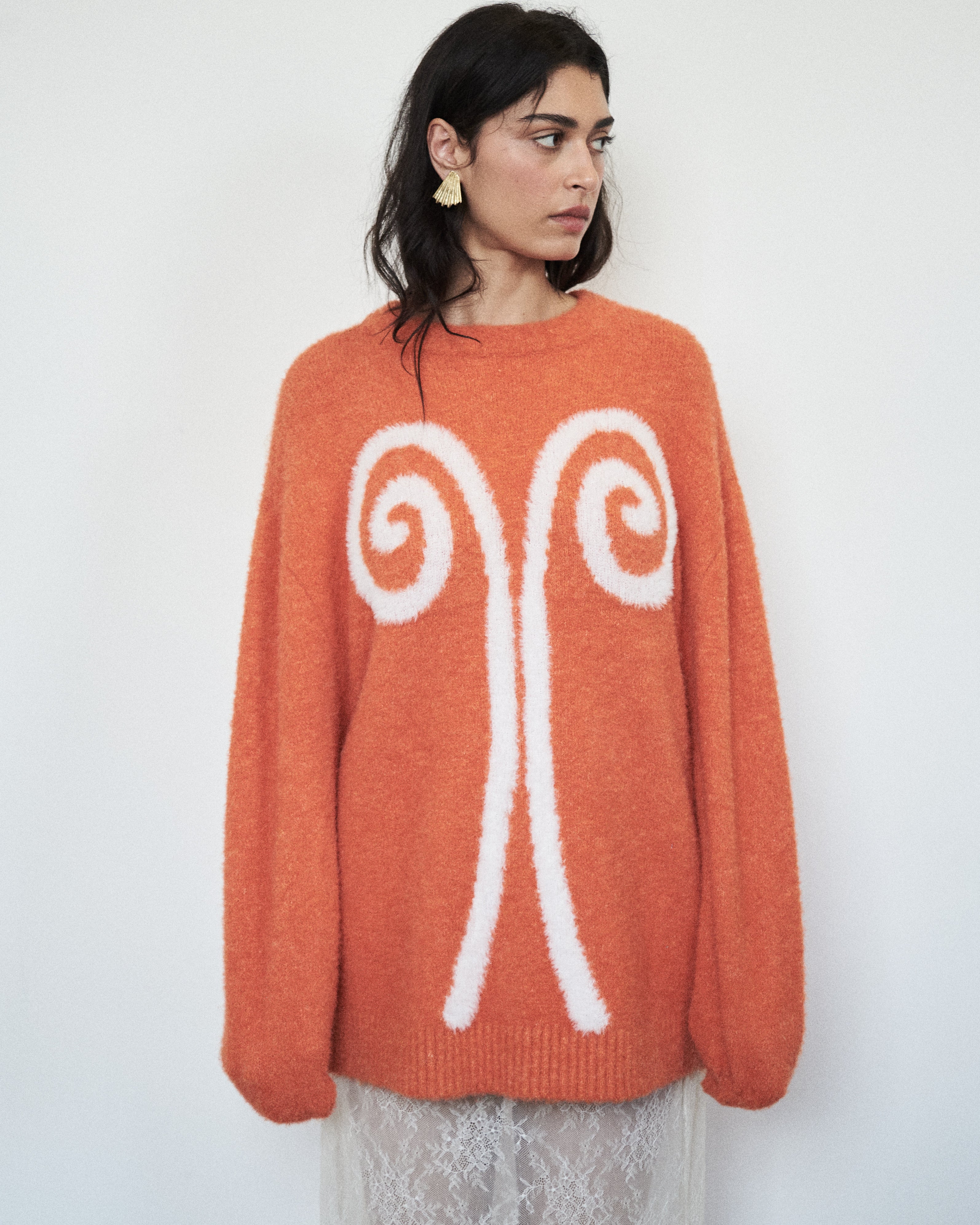 Editorial mood image of the VARNA Maris Knit Top in tangerine — designer alpaca-wool knit with voluminous sleeves and contrasting motif.