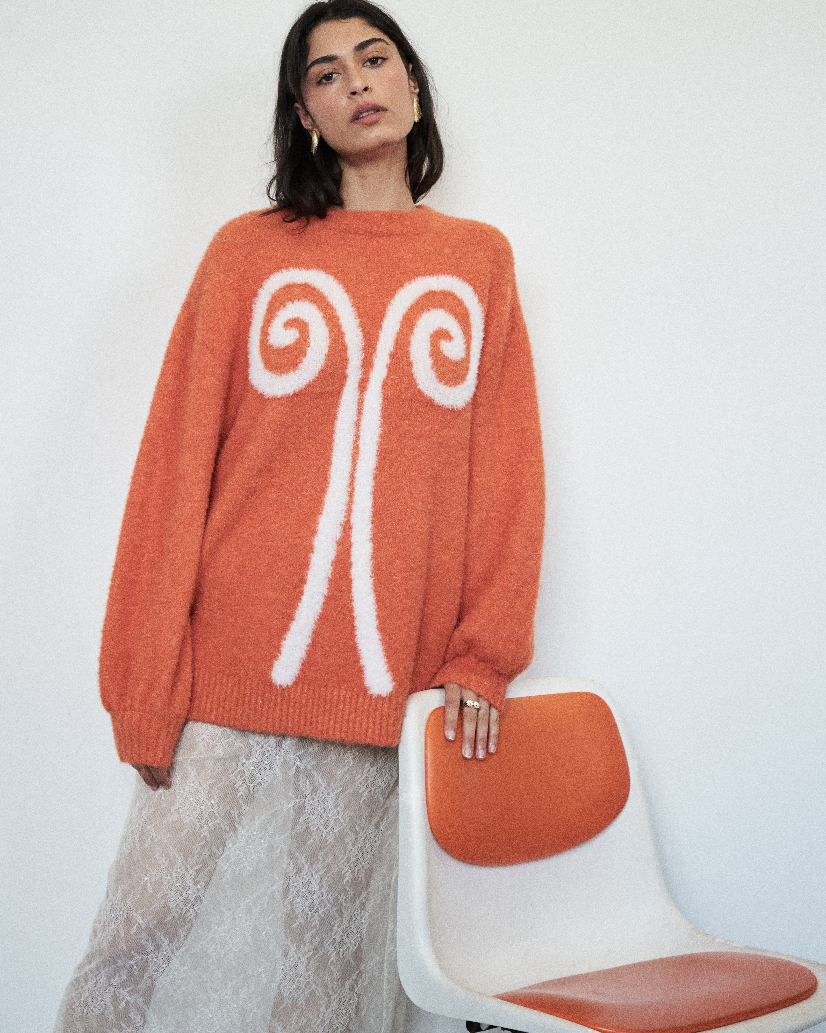 Moody editorial shot of the VARNA Maris Knit Top in tangerine — soft alpaca-wool texture and bold abstract motif.