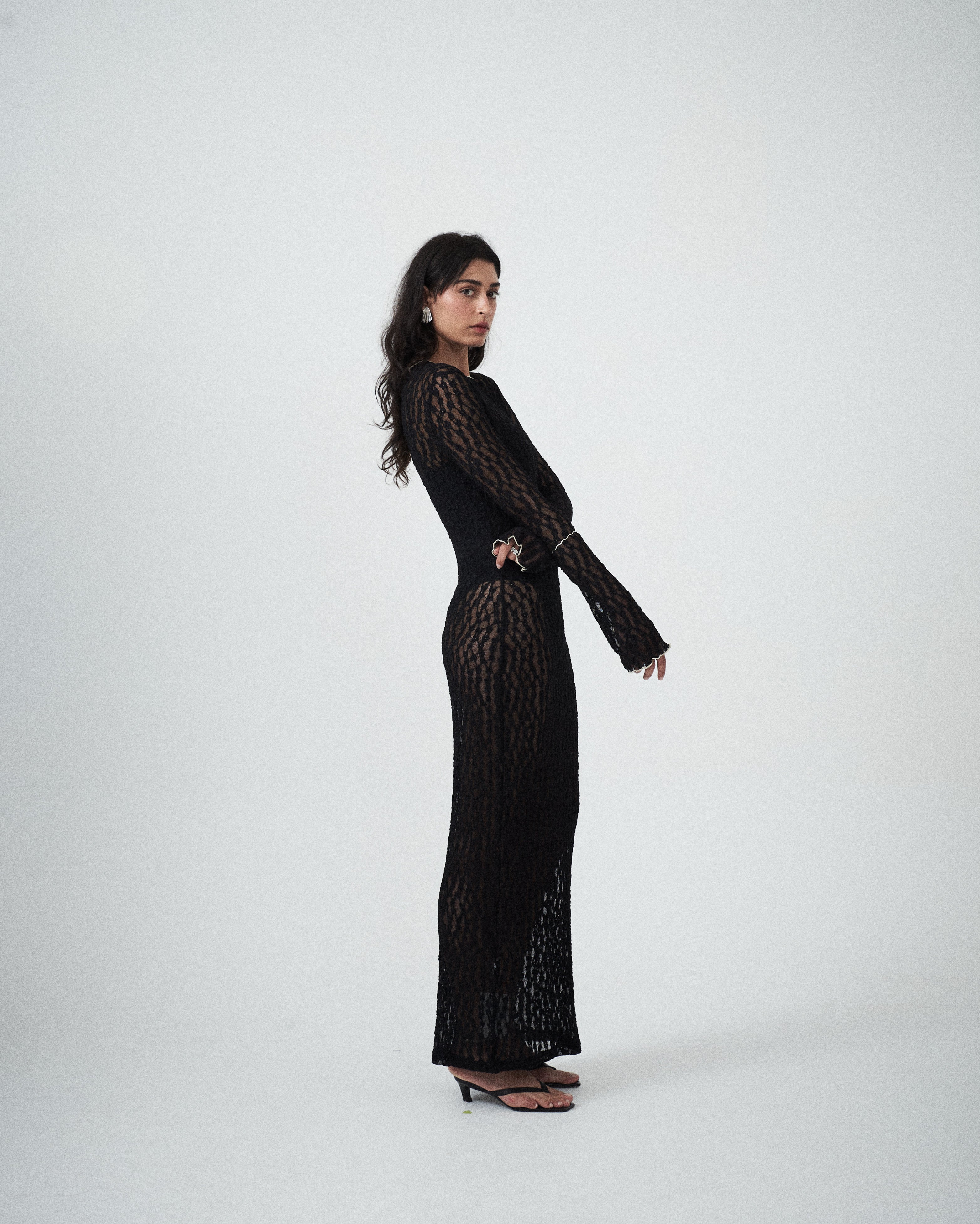 VARNA Cecil Maxi Dress styled in an editorial lookbook — sheer black lace dress with long sleeves and body-skimming silhouette.