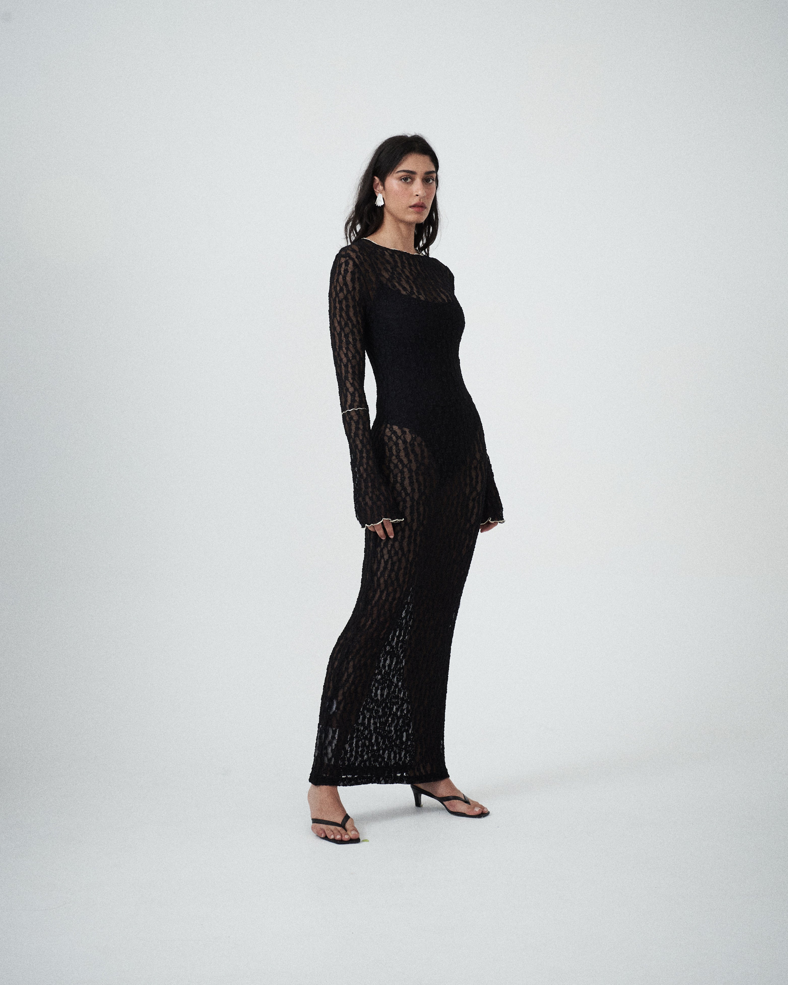 Three-quarter view of designer black lace maxi dress by VARNA showing slim silhouette and long sleeves.