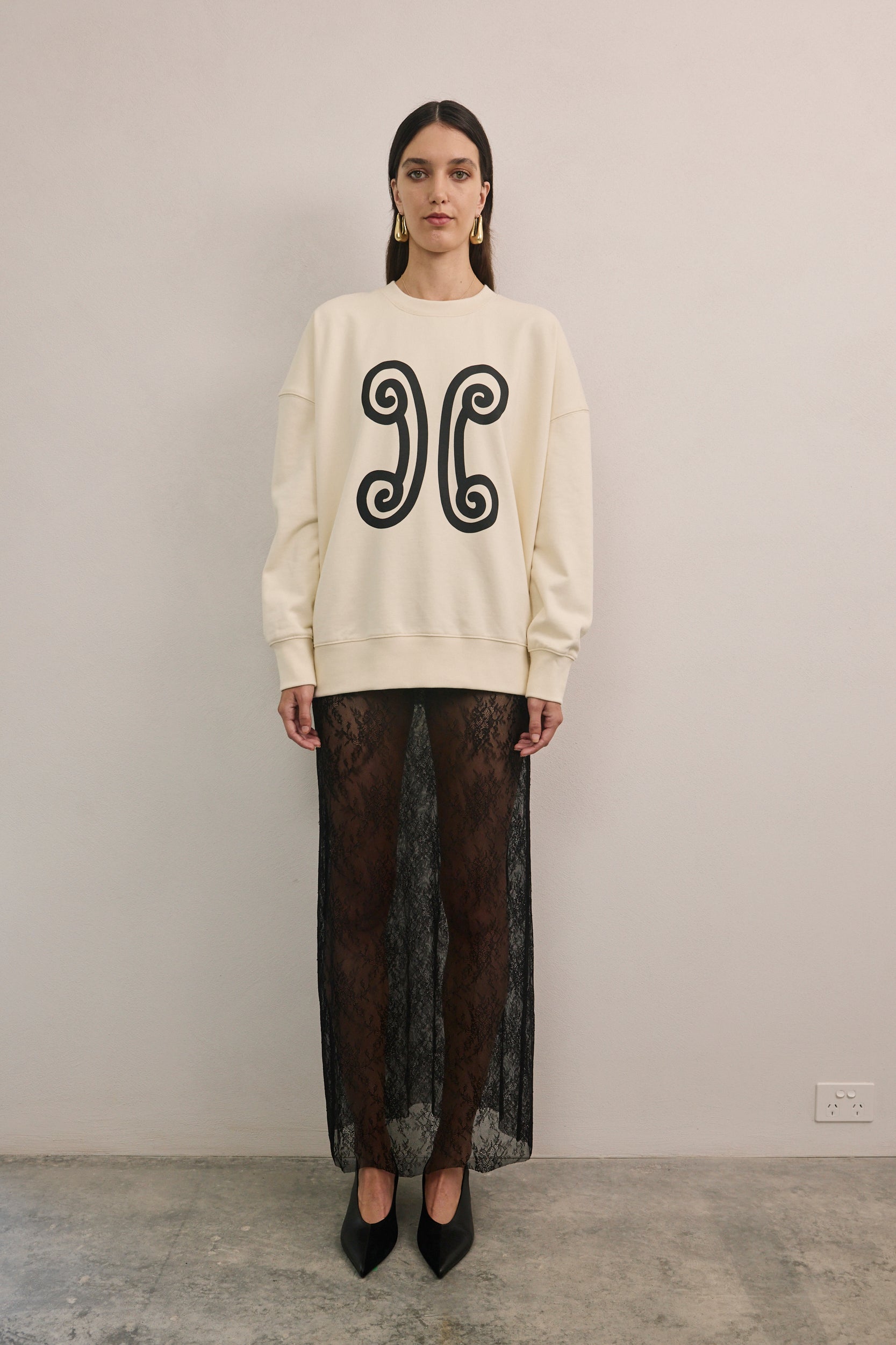 Close-up of VARNA Valencia Sweater showing printed emblem on soft ivory cotton.