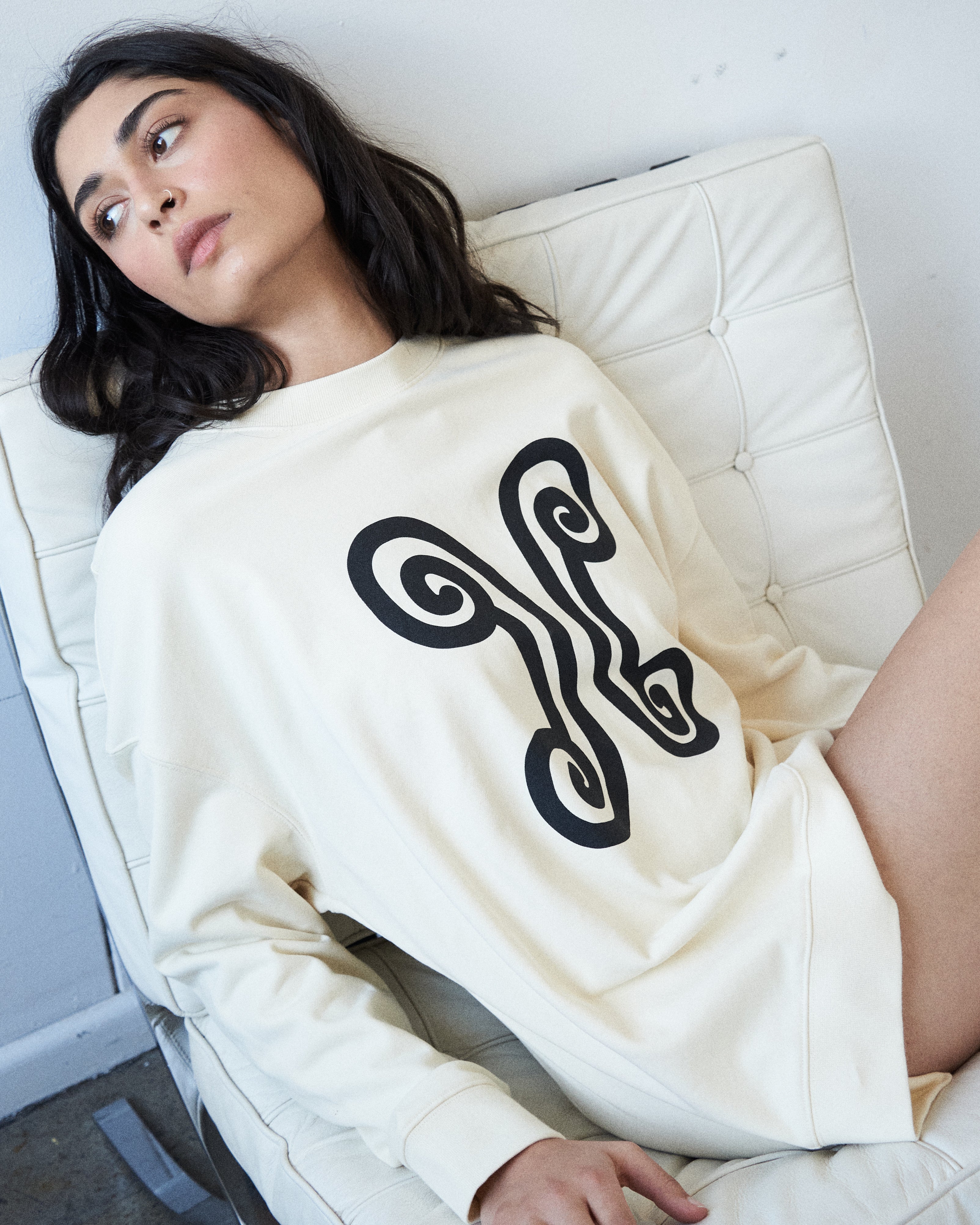 Designer oversized cotton sweater by VARNA with printed emblem in ivory.