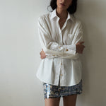 Editorial mood shot of the VARNA Rhea Shirt — designer white cotton button-down with gold-tone buttons and relaxed tailoring.