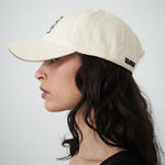 Designer women’s cream drill cap by VARNA featuring embroidered swirl emblem, side view