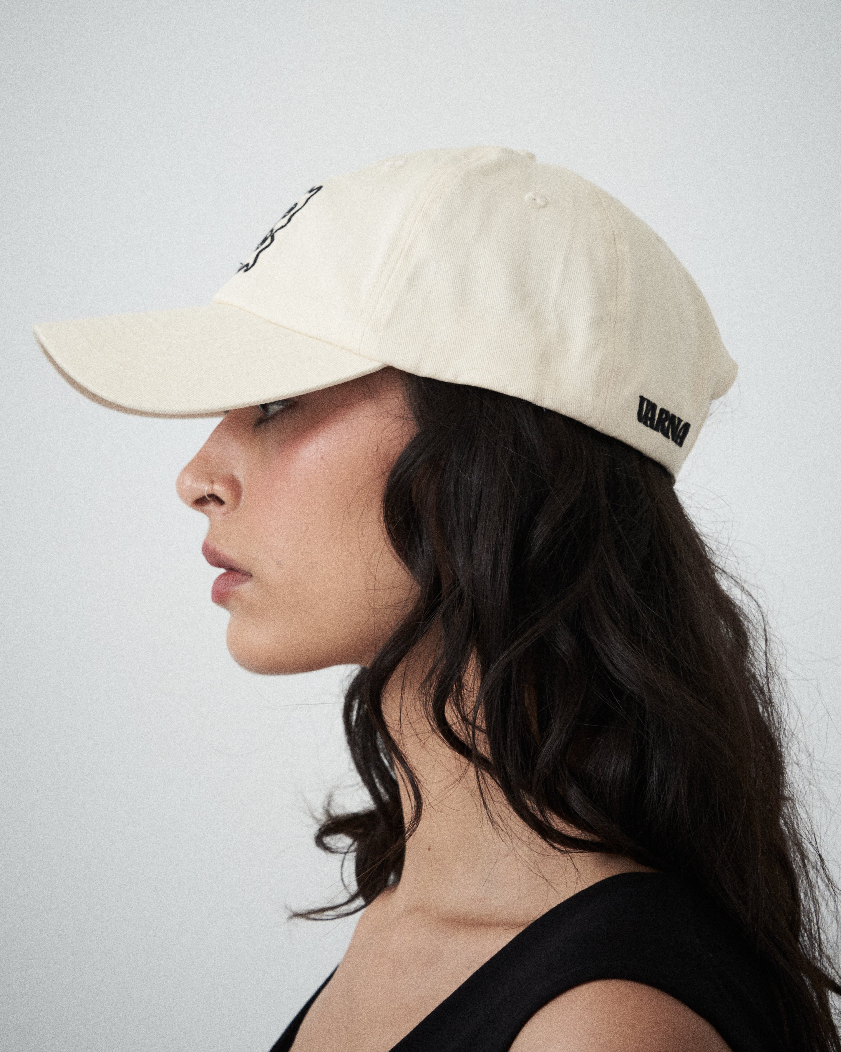 Designer women’s cream drill cap by VARNA featuring embroidered swirl emblem, side view