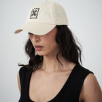 Designer women’s cream drill cap by VARNA featuring embroidered swirl emblem.