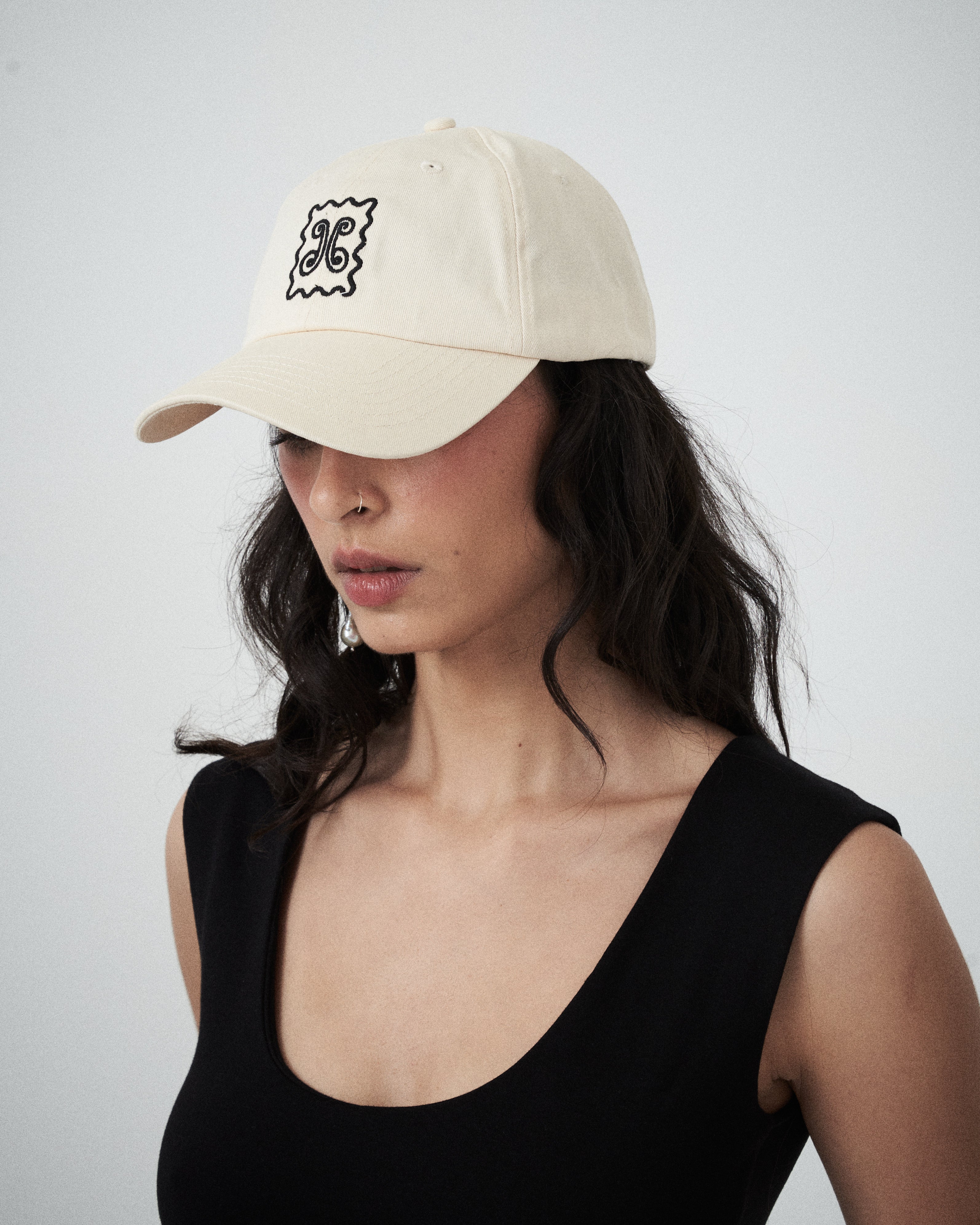 Designer women’s cream drill cap by VARNA featuring embroidered swirl emblem.