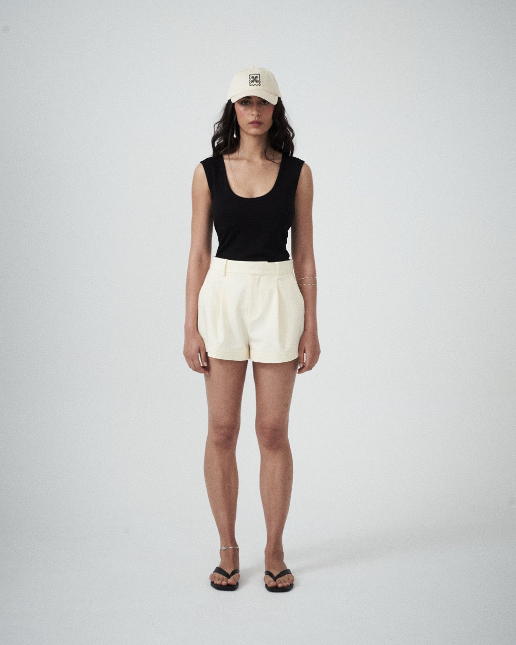 Person wearing a black sleeveless top and cream shorts on a plain background