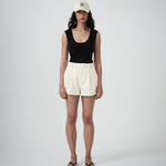 Person wearing a black sleeveless top and cream shorts on a plain background