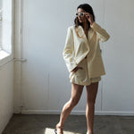 Woman in a cream-colored suit standing in a room with sunlight filtering through.