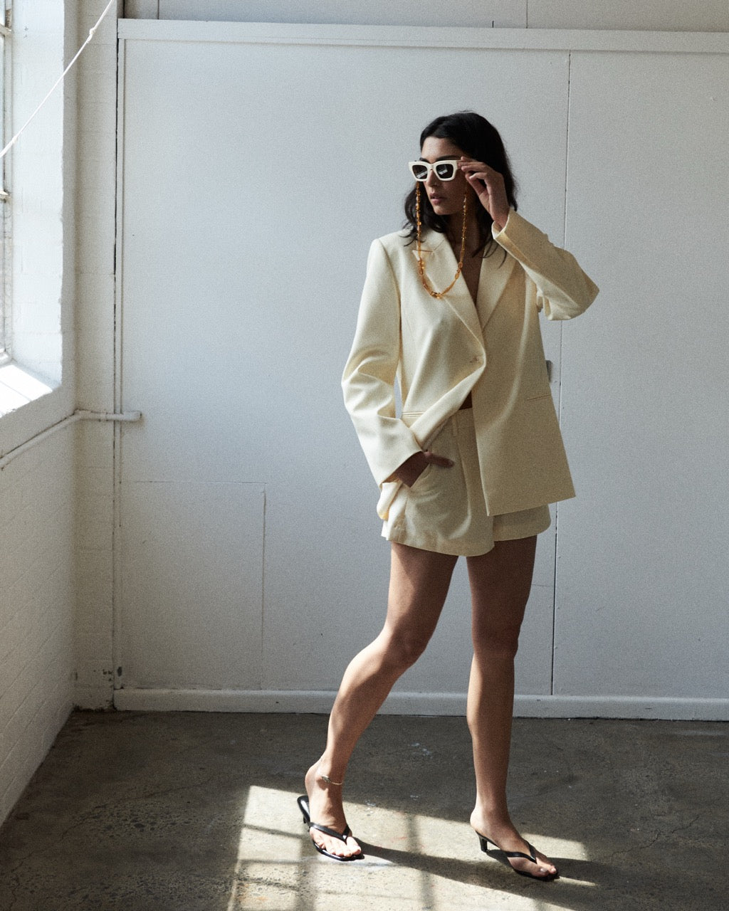 Woman in a cream-colored suit standing in a room with sunlight filtering through.