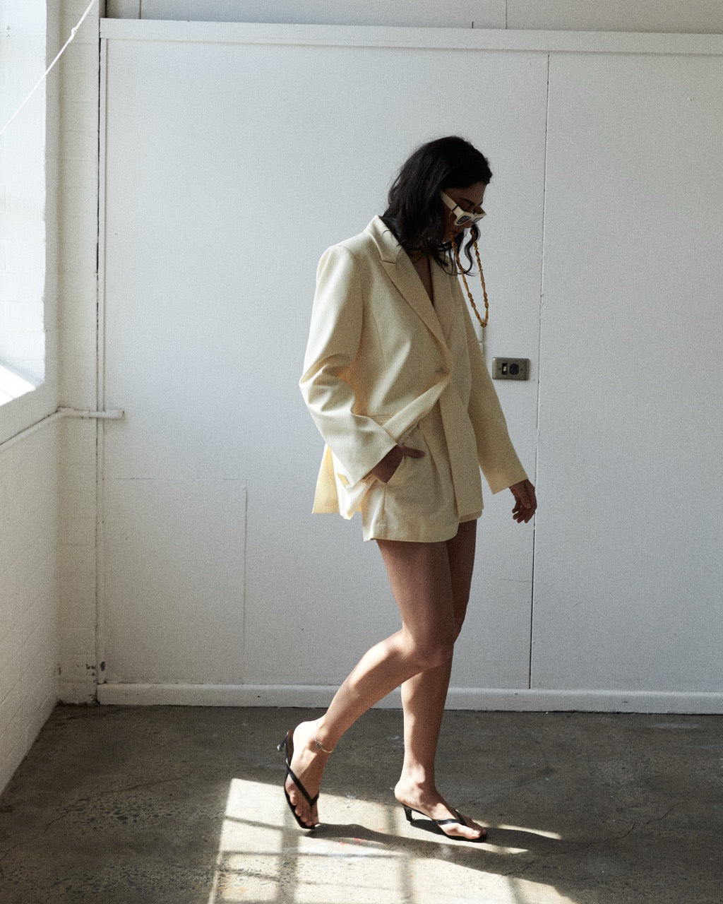 Person wearing a light-colored suit standing in a room with white walls and concrete floor.