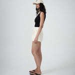 Woman wearing a black sleeveless top and cream shorts with pleats on a plain background