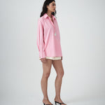 Woman wearing a pink shirt and white shorts on a plain background