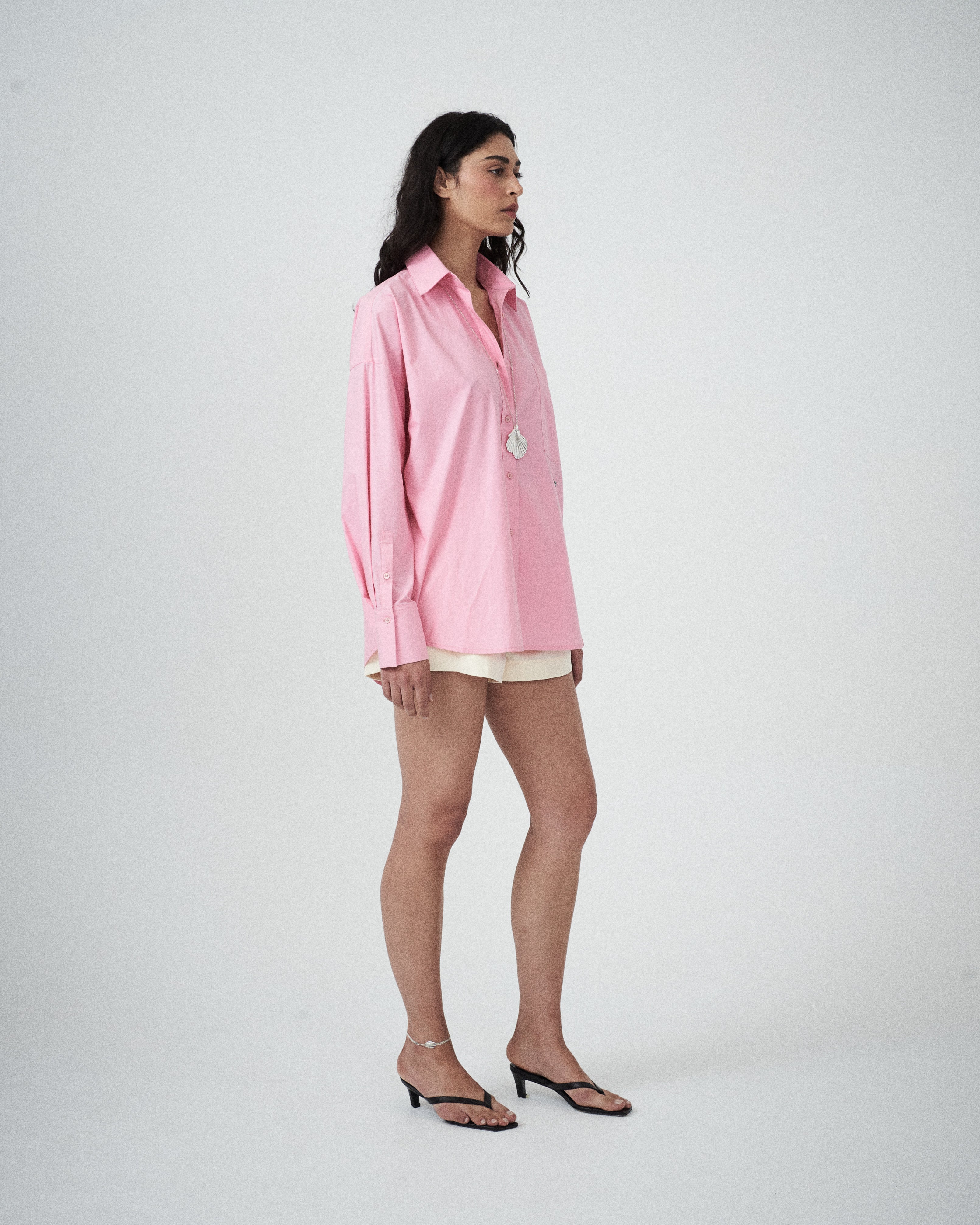 Woman wearing a pink shirt and white shorts on a plain background