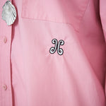 Pink shirt with a decorative emblem and shell pendant.