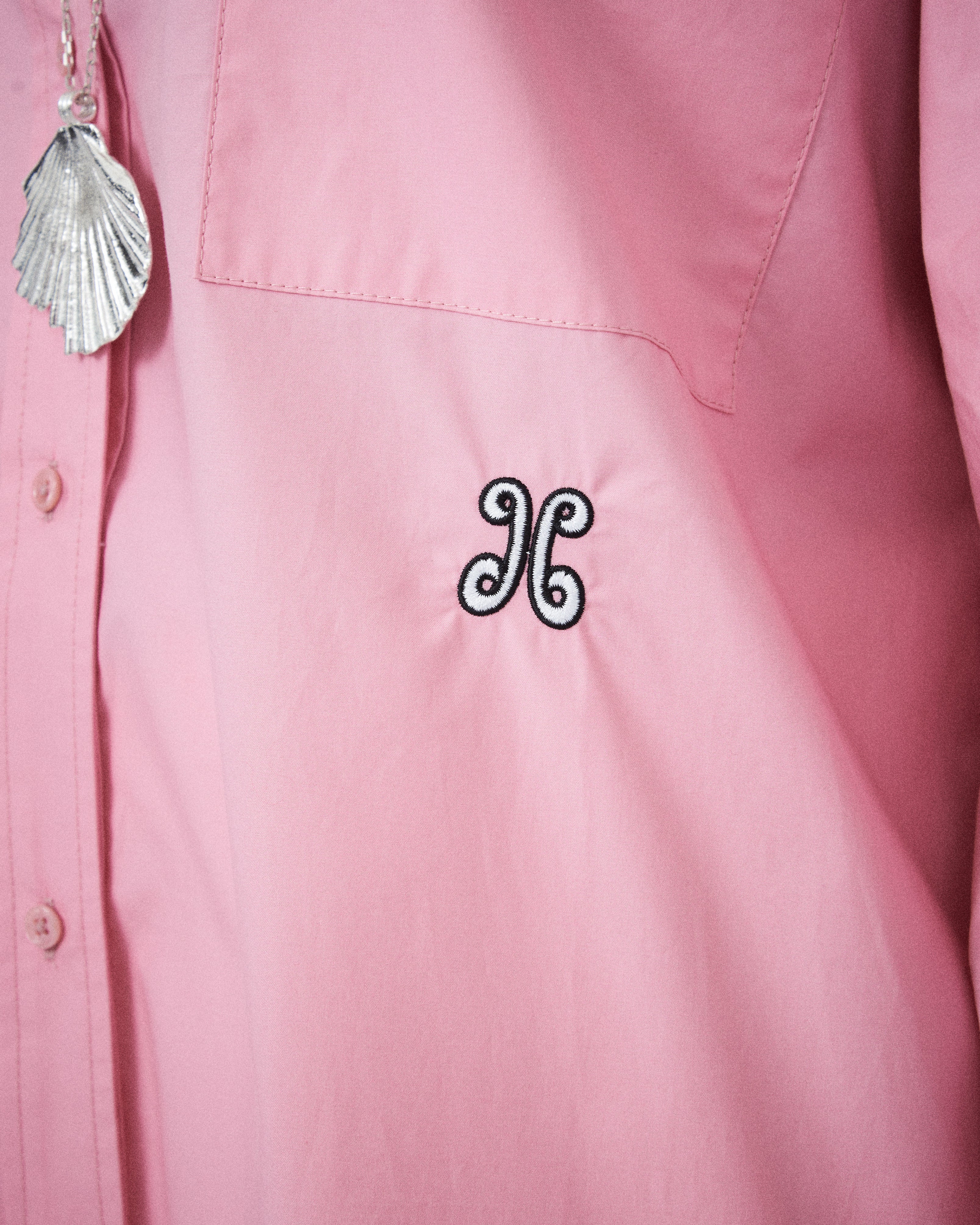 Pink shirt with a decorative emblem and shell pendant.