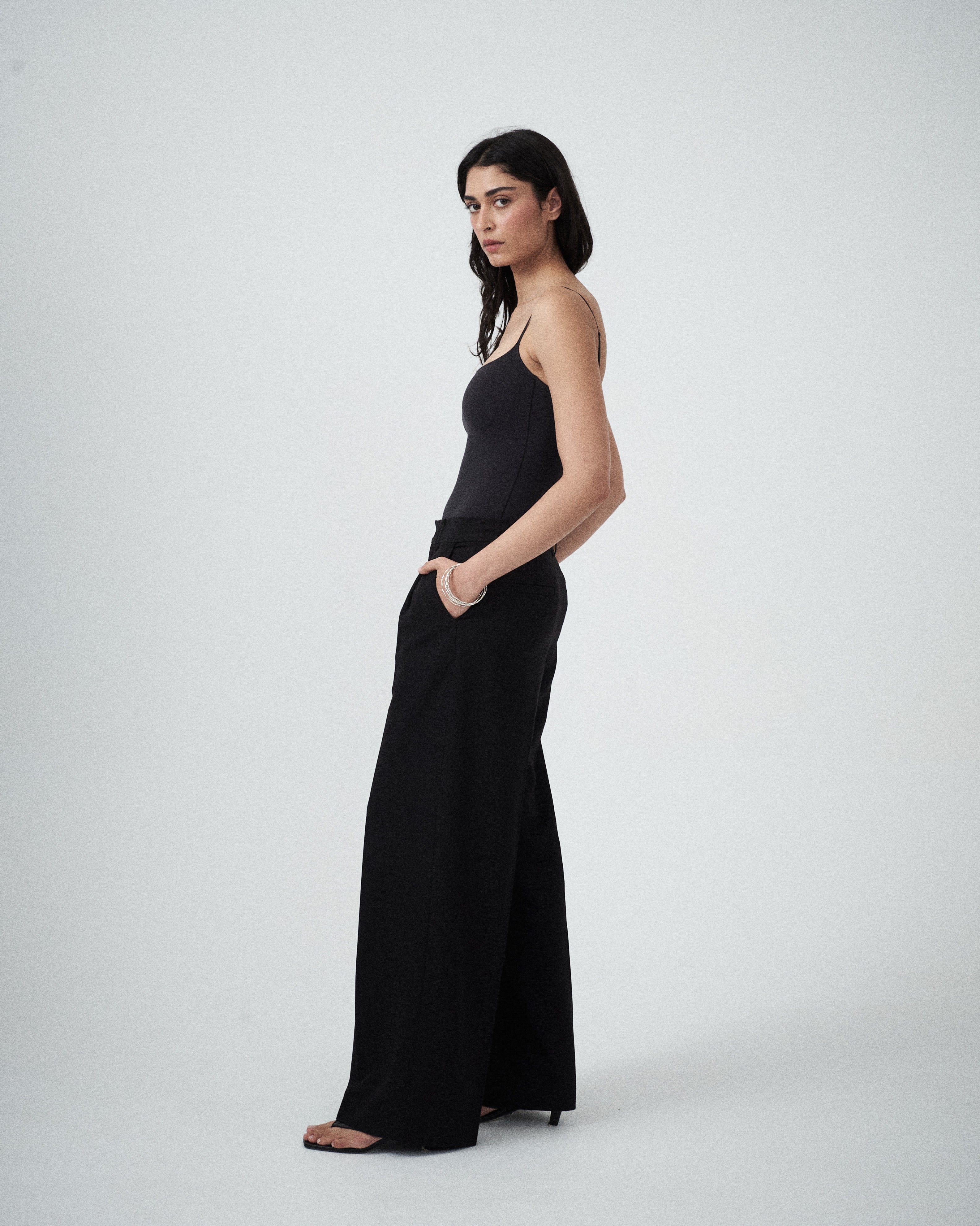 Three-quarter view of VARNA Enrica Relaxed Tailored Pant in black highlighting fluid drape and tailored silhouette.