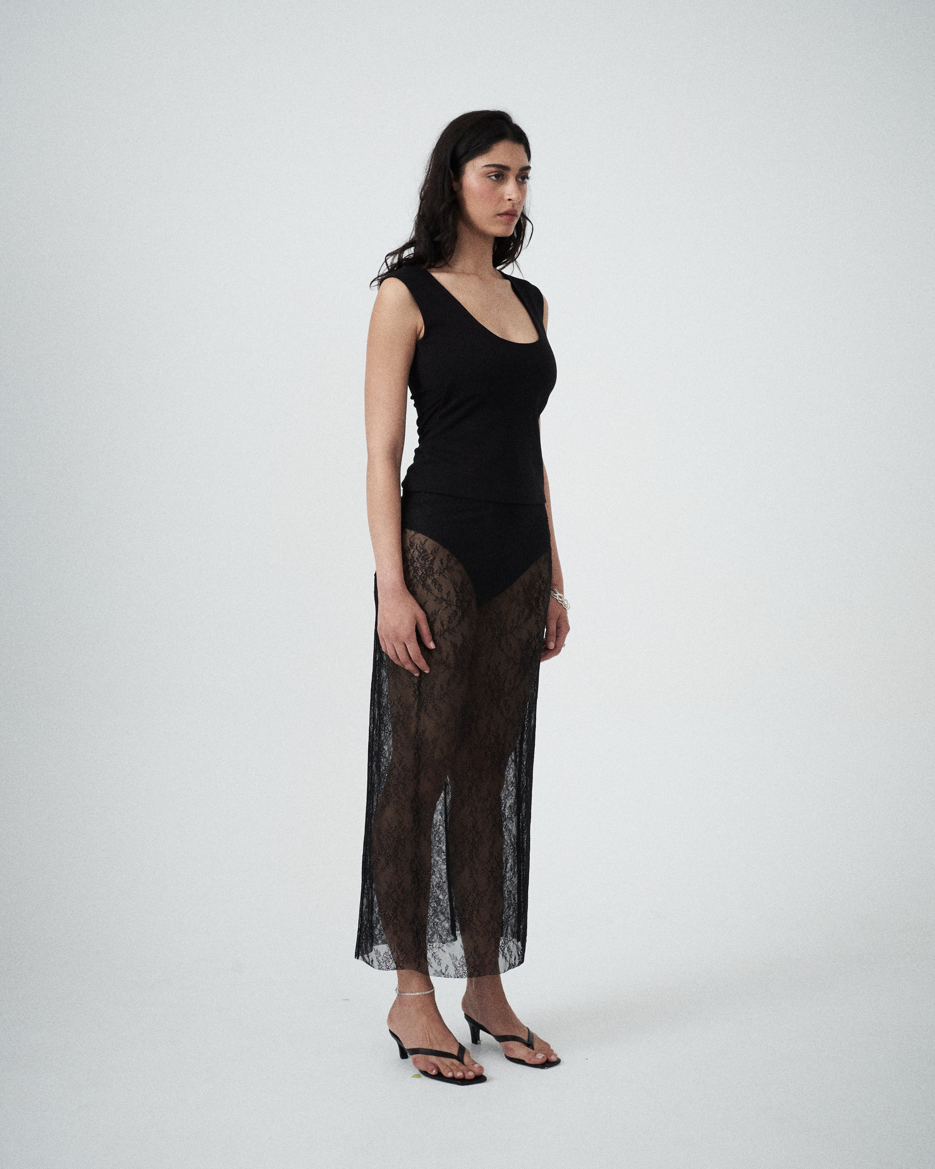 Side profile of VARNA Lucienne Maxi Lace Skirt in black — sheer floral lace fabric highlighting graceful drape and straight silhouette.