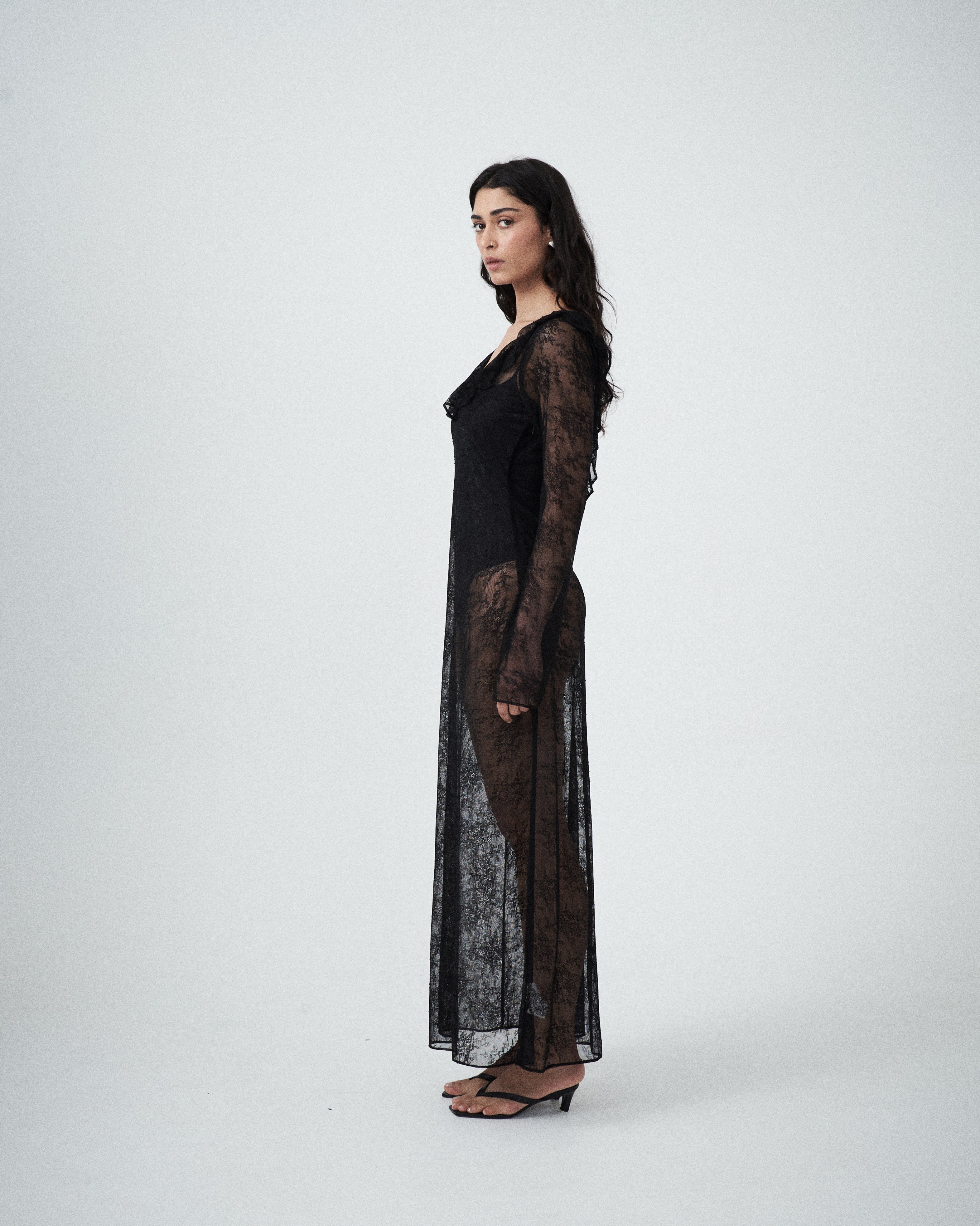 Side profile of VARNA Lucienne Ruffle Lace Maxi Dress in black showing sheer lace texture and graceful drape.