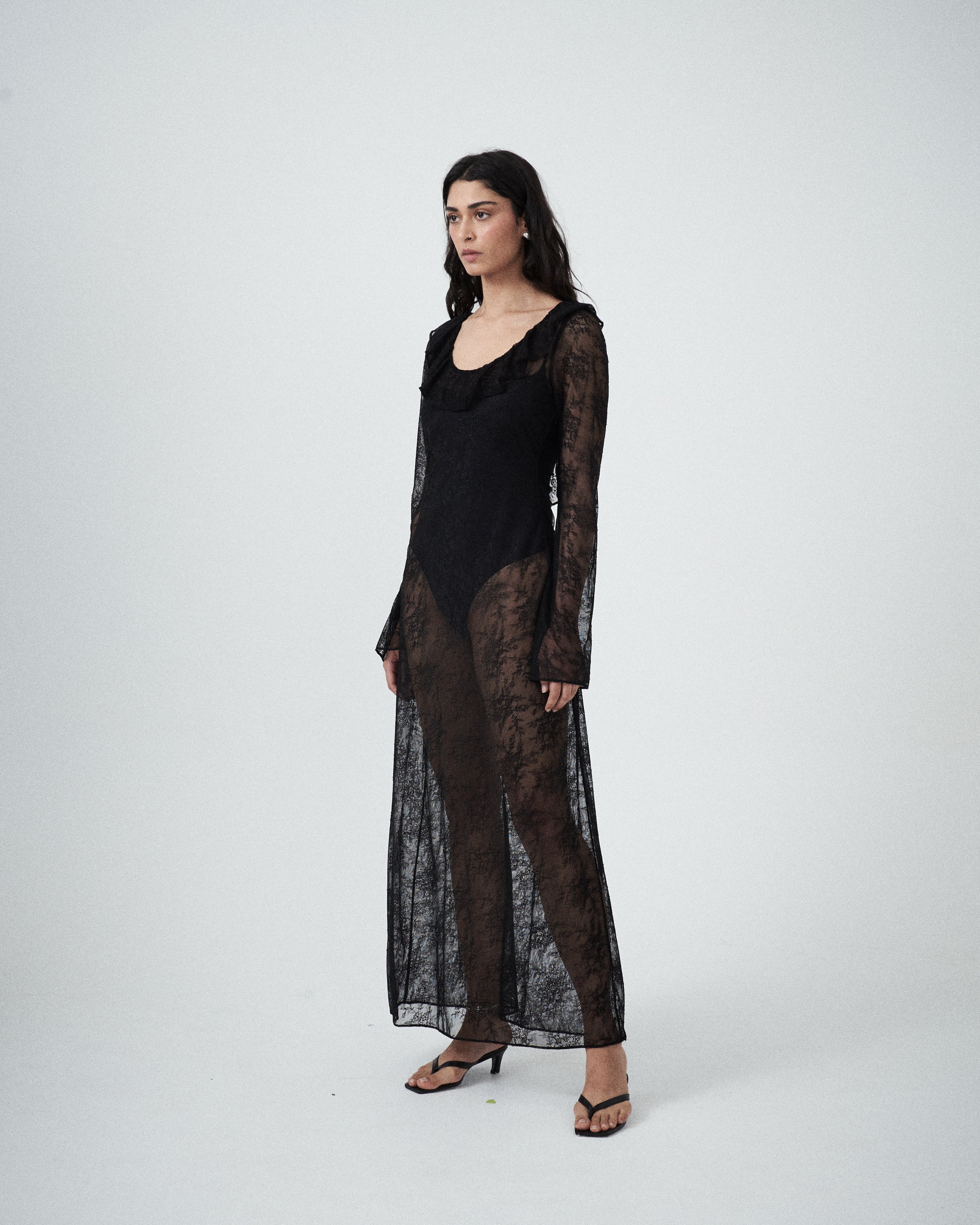 Three-quarter view of VARNA Lucienne Ruffle Lace Maxi Dress in black highlighting fluted sleeves and low back tie.