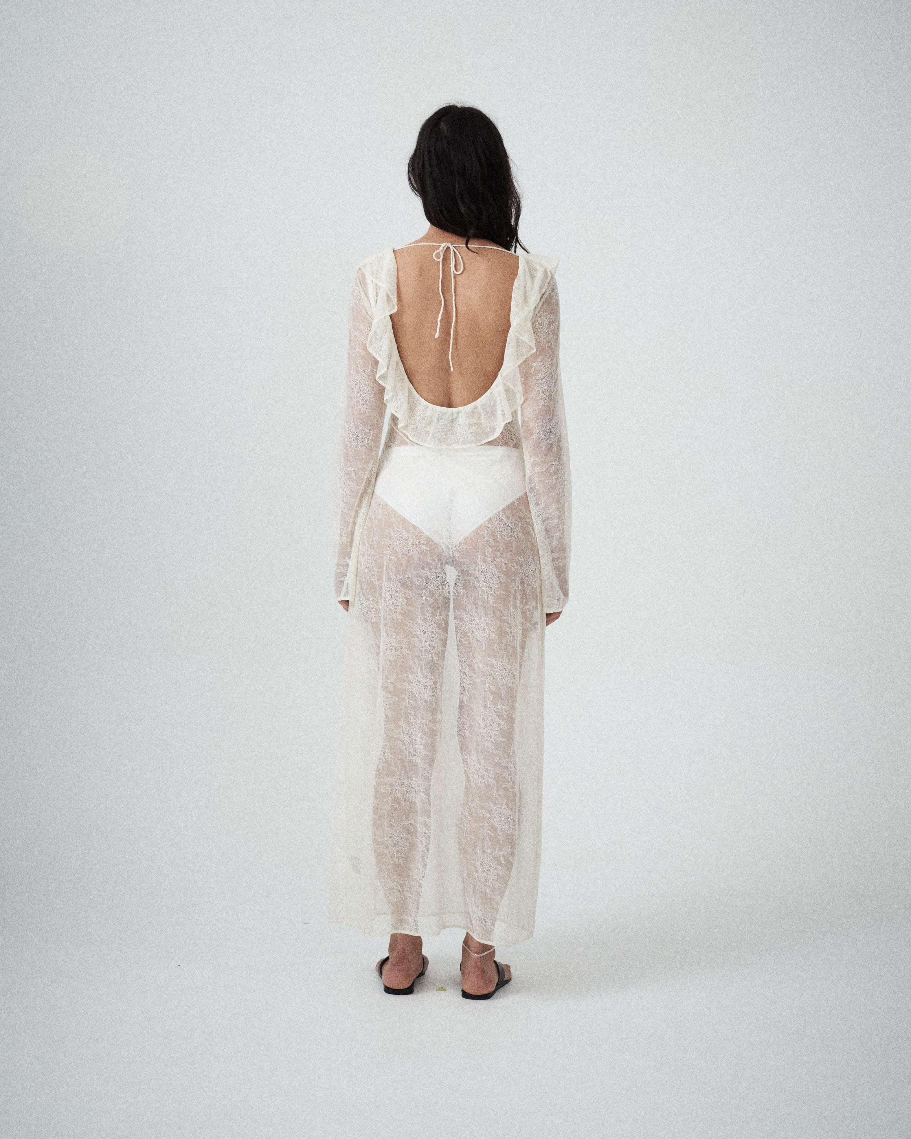 Back view of VARNA Lucienne Ruffle Lace Maxi Dress in milk featuring open low back with tie and soft ruffled hem.
