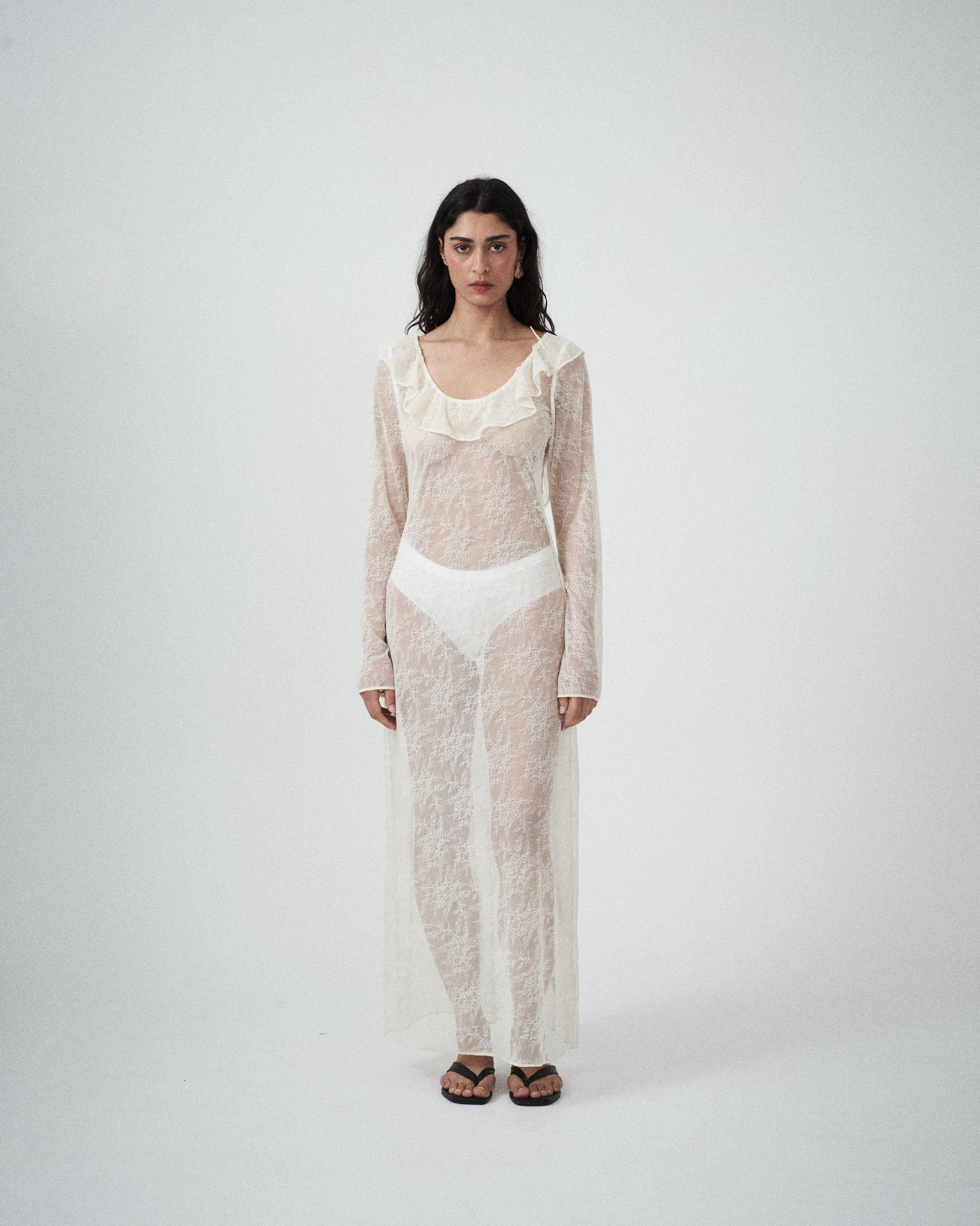 Front view of VARNA Lucienne Ruffle Lace Maxi Dress in milk styled with bra and briefs — sheer lace texture and fluted sleeves.