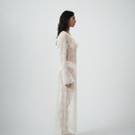 Side profile of VARNA Lucienne Ruffle Lace Maxi Dress in milk highlighting fluted sleeves, low back, and flowing lace silhouette.