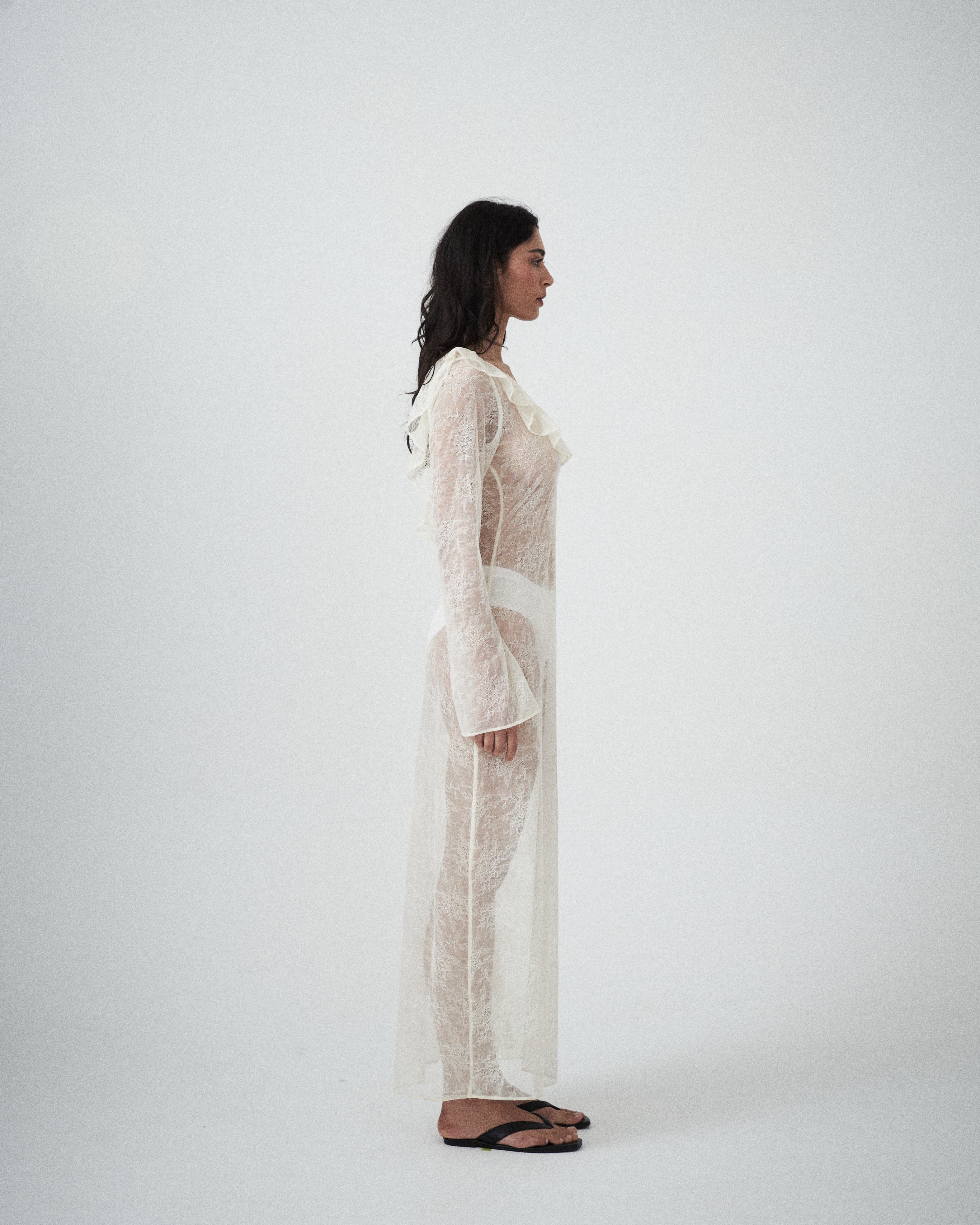 Side profile of VARNA Lucienne Ruffle Lace Maxi Dress in milk highlighting fluted sleeves, low back, and flowing lace silhouette.