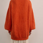 Back view of VARNA Maris Knit Top in tangerine alpaca-wool blend highlighting oversized silhouette and ribbed cuffs.