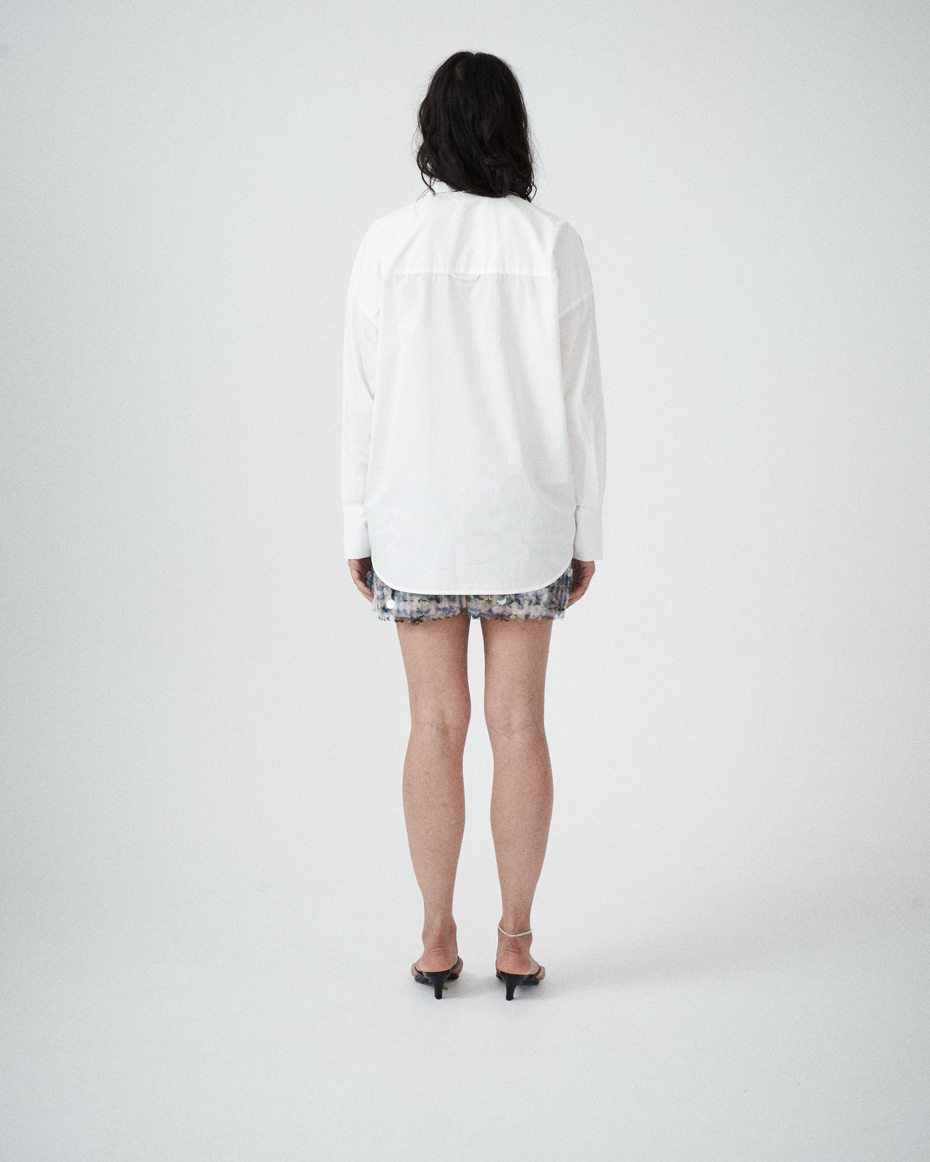 Back view of VARNA Rhea Shirt in crisp white cotton with subtle drop shoulders and gold-tone buttons.