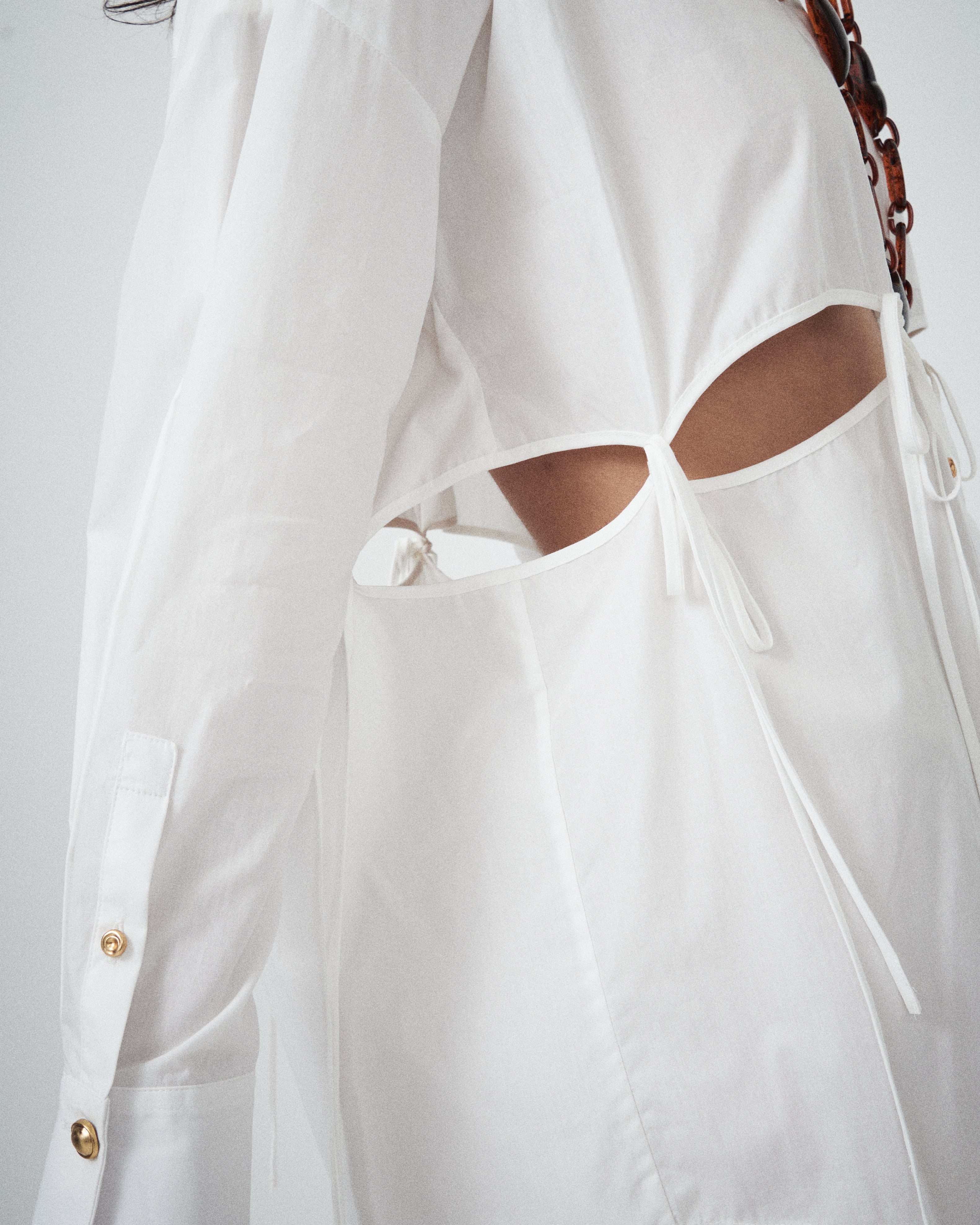 Crisp white cotton fabric of VARNA Rhea Tied Shirt with gold-tone buttons and tie details.